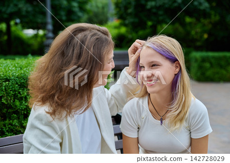 Loving mother touching her teenage daughter hair tenderly on park bench Loving mother touching her teenage daughter hair tenderly on park bench 142728029