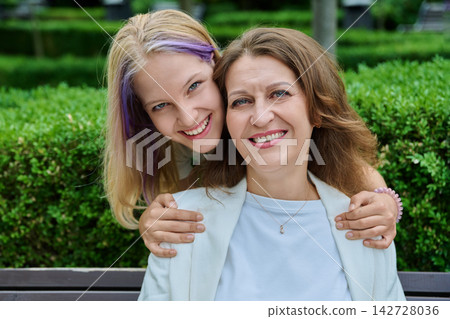 Close up portrait of mother and teenage daughter hugging from behind park Close up portrait of mother and teenage daughter hugging from behind park 142728036