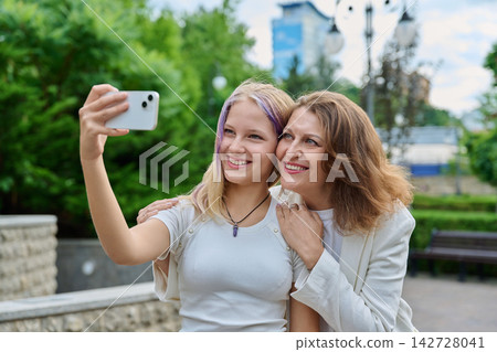 Happy mother and daughter taking selfie photo with smartphone outdoors in park Happy mother and daughter taking selfie photo with smartphone outdoors in park 142728041