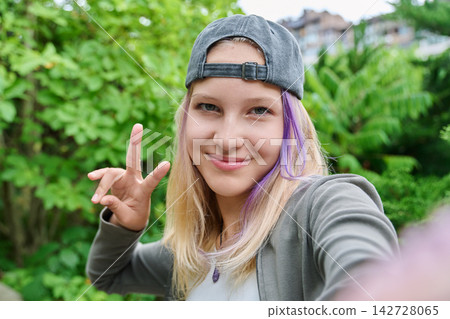 Cheerful teenage girl taking selfie showing peace sign outdoors close up Cheerful teenage girl taking selfie showing peace sign outdoors close up 142728065
