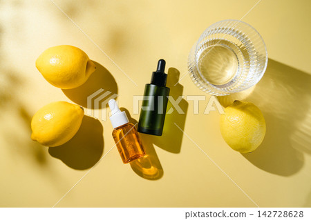 Cosmetic dropper bottles with glass of water and fresh lemon fruits in bright sunlight, clean beauty and skincare concept, top view on yellow background Cosmetic dropper bottles with glass of water and fresh lemon fruits in bright sunlight, clean beauty and skincare concept, top view on yellow background 142728628