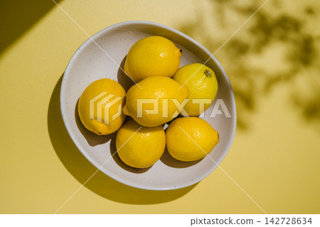 Fresh lemons in ceramic bowl on yellow background, vibrant citrus fruit still life with copy space Fresh lemons in ceramic bowl on yellow background, vibrant citrus fruit still life with copy space 142728634