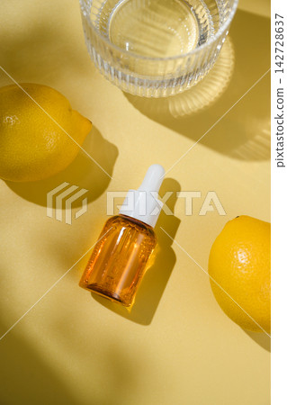 Vitamin C serum in amber dropper bottle with fresh lemons and glass of water on yellow background, bright natural skincare concept Vitamin C serum in amber dropper bottle with fresh lemons and glass of water on yellow background, bright natural skincare concept 142728637