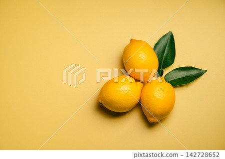 Three fresh lemons with green leaves on yellow background, bright citrus fruit still life with generous copy space Three fresh lemons with green leaves on yellow background, bright citrus fruit still life with generous copy space 142728652