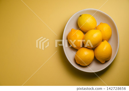 Fresh lemons in ceramic bowl on yellow background, overhead citrus fruit still life with bright copy space Fresh lemons in ceramic bowl on yellow background, overhead citrus fruit still life with bright copy space 142728656