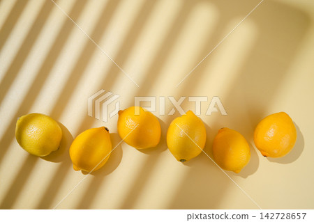 Fresh lemons arranged in a row with dramatic window light and shadows on warm yellow background, vibrant citrus still life 142728657
