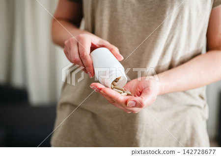 Woman pouring a pile of pills, capsules from a bottle in hand. Prescription medication, treatment sickness concept 142728677