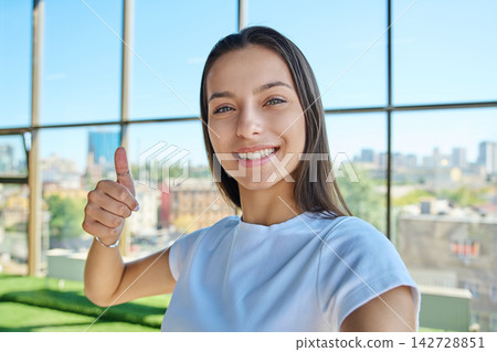 Young smiling woman showing thumb up hand sign while taking selfie photo 142728851