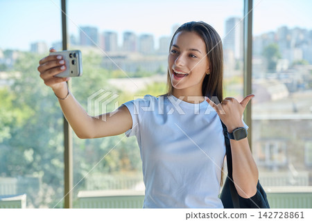Smiling female student taking selfie photo showing shaka sign city window Smiling female student taking selfie photo showing shaka sign city window 142728861