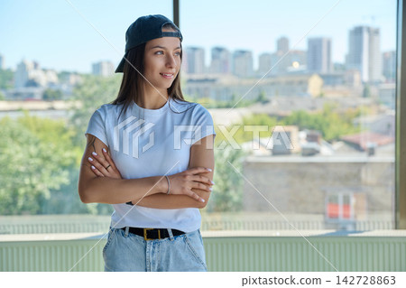 Young woman in backward cap standing arms crossed looking away Young woman in backward cap standing arms crossed looking away 142728863