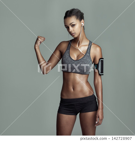 Studio portrait, woman and muscle flex for exercise with power, strong arm and earphones for kpop music playlist. Athlete girl, strength and audio sound by gray background for workout and podcast Studio portrait, woman and muscle flex for exercise with power, strong arm and earphones for kpop music playlist. Athlete girl, strength and audio sound by gray background for workout and podcast 142728907
