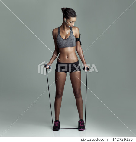 Woman, music and skipping rope for workout in studio for exercise, health or fitness on gray background. Female athlete, fashion and earphones or equipment for determination, wellbeing or motivation Woman, music and skipping rope for workout in studio for exercise, health or fitness on gray background. Female athlete, fashion and earphones or equipment for determination, wellbeing or motivation 142729156