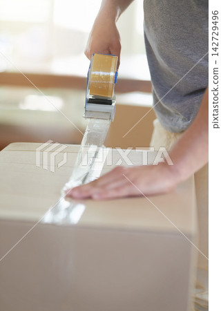 Person, hands and packing tape for cardboard box or package on moving day for real estate and new home. Homeowner, house relocation and property with closing parcel or cargo for item storage Person, hands and packing tape for cardboard box or package on moving day for real estate and new home. Homeowner, house relocation and property with closing parcel or cargo for item storage 142729496