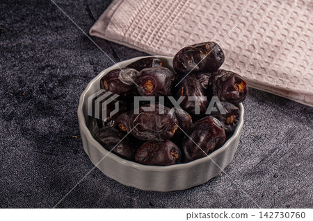 Dark brown dates in textured gray ceramic bowl on dark stone surface with folded beige napkin background Dark brown dates in textured gray ceramic bowl on dark stone surface with folded beige napkin background 142730760