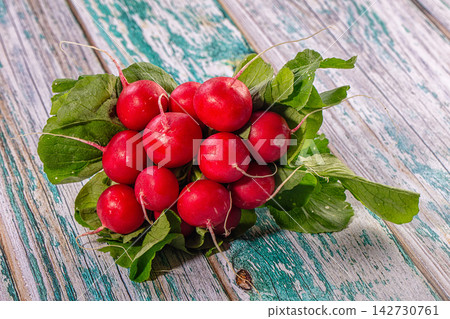 Fresh red radishes with green leaves on weathered teal and gray wooden surface, natural lighting, rustic food composition Fresh red radishes with green leaves on weathered teal and gray wooden surface, natural lighting, rustic food composition 142730761