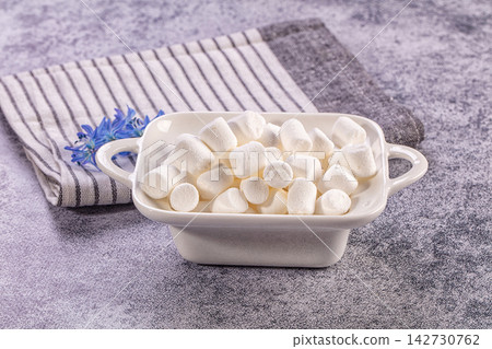 White marshmallows in ceramic dish on textured purple surface with striped cloth and blue flower accent White marshmallows in ceramic dish on textured purple surface with striped cloth and blue flower accent 142730762