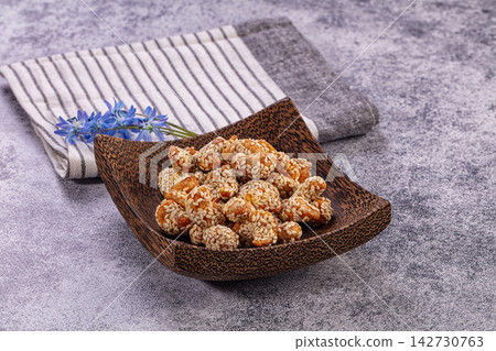 Sesame coated snack pieces in wooden bowl with blue flowers and striped cloth on textured gray surface 142730763
