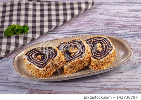 Three slices of sesame coated sweet roll with swirl pattern, chopped nuts, served on ceramic plate with checkered cloth and mint leaf Three slices of sesame coated sweet roll with swirl pattern, chopped nuts, served on ceramic plate with checkered cloth and mint leaf 142730787