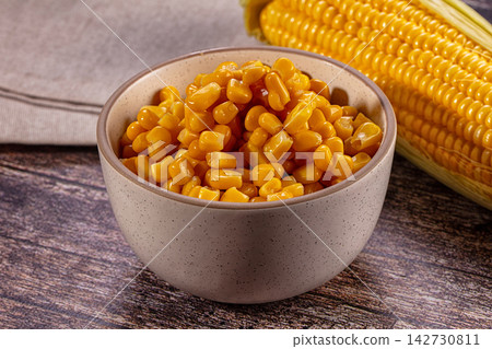 Fresh yellow corn kernels in speckled ceramic bowl beside whole corn cob on rustic wooden table with linen napkin Fresh yellow corn kernels in speckled ceramic bowl beside whole corn cob on rustic wooden table with linen napkin 142730811