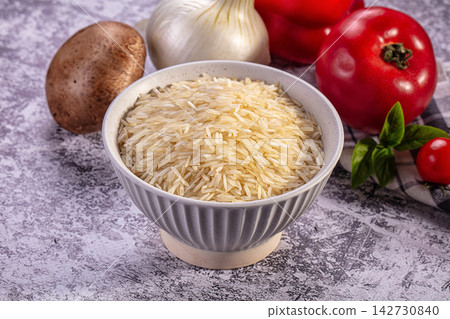 Bowl of uncooked rice with fresh tomato mushroom garlic and basil on textured surface 142730840