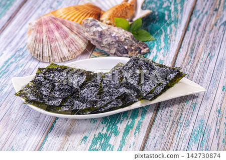 Crispy nori sheets on white plate with scallop shells and oyster on weathered teal wooden background, shallow depth of field 142730874