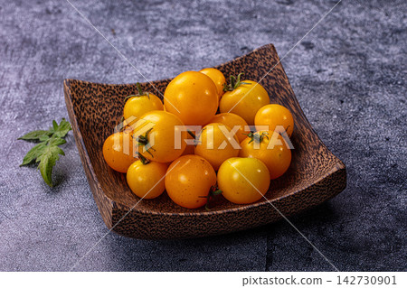 Yellow cherry tomatoes in rustic wooden bowl on dark textured surface with fresh green leaf beside Yellow cherry tomatoes in rustic wooden bowl on dark textured surface with fresh green leaf beside 142730901