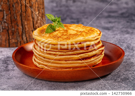 Stack of golden pancakes on wooden plate with fresh mint garnish, rustic tree trunk background, warm natural lighting Stack of golden pancakes on wooden plate with fresh mint garnish, rustic tree trunk background, warm natural lighting 142730966