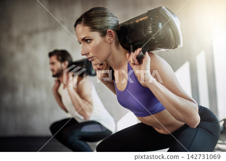 Squat, sandbag and fitness exercise or gym class with personal trainer for training, weights or strength. Man, woman and glutes routine for muscle building or leg goals together, equipment or workout Squat, sandbag and fitness exercise or gym class with personal trainer for training, weights or strength. Man, woman and glutes routine for muscle building or leg goals together, equipment or workout 142731069