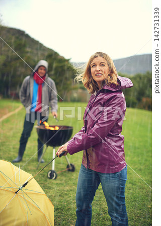 Wind, woman and rain at barbecue in outdoor on vacation or picnic as family in together. Female person, bad weather and struggle with umbrella for grill or bbq at celebration or event in Scotland Wind, woman and rain at barbecue in outdoor on vacation or picnic as family in together. Female person, bad weather and struggle with umbrella for grill or bbq at celebration or event in Scotland 142731339