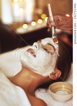 Woman, face mask and hand brush for spa treatment or beautician for vacation, stress relief or dermatology. Female person, calm and facial with candle bokeh at Bali resort in hotel, relax or skincare 142731340