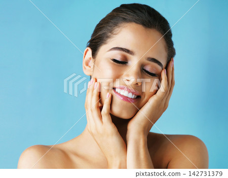 Happy woman, beauty and makeup with skincare in satisfaction for facial on a blue studio background. Face of calm female person or model with smile in relax for cosmetics, dermatology or cosmetology Happy woman, beauty and makeup with skincare in satisfaction for facial on a blue studio background. Face of calm female person or model with smile in relax for cosmetics, dermatology or cosmetology 142731379