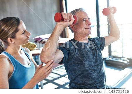 Elderly man, physiotherapist and exercise with dumbbell in clinic for rehabilitation, support or recovery. Fitness, female coach and senior patient on ball for help, balance strength or physiotherapy Elderly man, physiotherapist and exercise with dumbbell in clinic for rehabilitation, support or recovery. Fitness, female coach and senior patient on ball for help, balance strength or physiotherapy 142731456