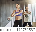 People, kettlebell and training together at gym, weightlifting and equipment for power workout. Man, woman and coach for athletes in health club, cardio fitness and friends support for exercise 142731537