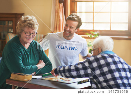Volunteer, man and happy with senior people in retirement home, board game and social interaction for advocacy. Male assistant, elderly women and scrabble for volunteering and community service. 142731956