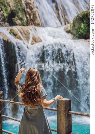 Woman traveler admiring El Chiflon waterfall from a wooden viewpoint in Chiapas Mexico with wooden railings tropical forest clear blue water nature travel and looking at the waterfall. Woman traveler admiring El Chiflon waterfall from a wooden viewpoint in Chiapas Mexico with wooden railings tropical forest clear blue water nature travel and looking at the waterfall. 142732072