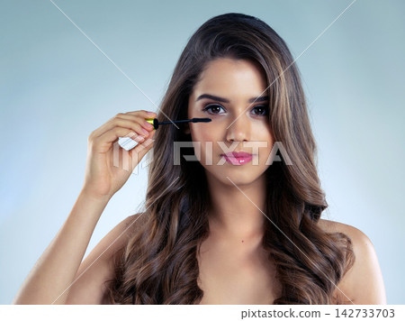 Beauty, makeup and mascara with portrait of woman in studio on blue background for aesthetic wellness. Brush, cosmetics and face with confident model at salon for dermatology or makeover treatment Beauty, makeup and mascara with portrait of woman in studio on blue background for aesthetic wellness. Brush, cosmetics and face with confident model at salon for dermatology or makeover treatment 142733703