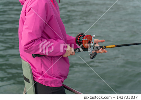 Close-up of female angler using fishing rod and reel during a Kamchatka sea trip. Recreational fishing, marine journey, outdoor leisure, active travel, adventure and tourism. Close-up of female angler using fishing rod and reel during a Kamchatka sea trip. Recreational fishing, marine journey, outdoor leisure, active travel, adventure and tourism. 142733837