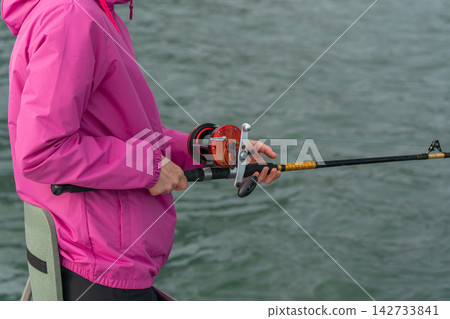 Close view of woman holding fishing rod and reel on a boat in Kamchatka. Sea trip, recreational fishing, travel lifestyle, outdoor leisure, marine adventure and active tourism. Close view of woman holding fishing rod and reel on a boat in Kamchatka. Sea trip, recreational fishing, travel lifestyle, outdoor leisure, marine adventure and active tourism. 142733841