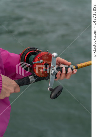 Close-up of hands holding fishing rod with reel during sea fishing trip. Recreational fishing, angling equipment, outdoor leisure, active travel, marine adventure and sport fishing Close-up of hands holding fishing rod with reel during sea fishing trip. Recreational fishing, angling equipment, outdoor leisure, active travel, marine adventure and sport fishing 142733858