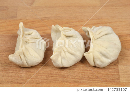 Three pleated dumplings on a wooden board Three pleated dumplings on a wooden board 142735107