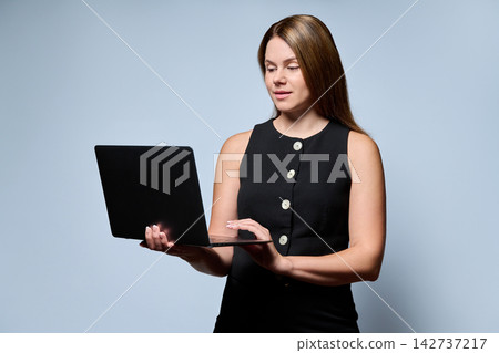 Businesswoman holding laptop and typing on light blue background Businesswoman holding laptop and typing on light blue background 142737217