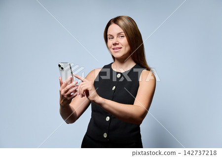 Businesswoman holding smartphone looking at camera isolated on light gray background Businesswoman holding smartphone looking at camera isolated on light gray background 142737218