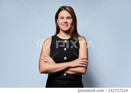 Smiling businesswoman standing with arms crossed on light blue background Smiling businesswoman standing with arms crossed on light blue background 142737224