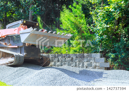 Construction equipment moves gravel in yard surrounded by trees Construction equipment moves gravel in yard surrounded by trees 142737394