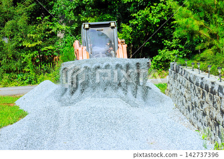 Excavator spreading gravel on path in wooded area during construction Excavator spreading gravel on path in wooded area during construction 142737396