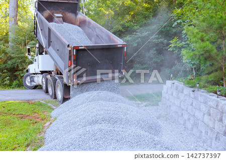 Truck unloads gravel beside stone wall in wooded area Truck unloads gravel beside stone wall in wooded area 142737397