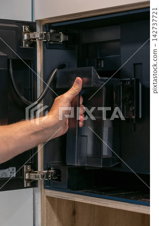 Hand removing water reservoir from built-in coffee machine in modern kitchen cabinet 142737721