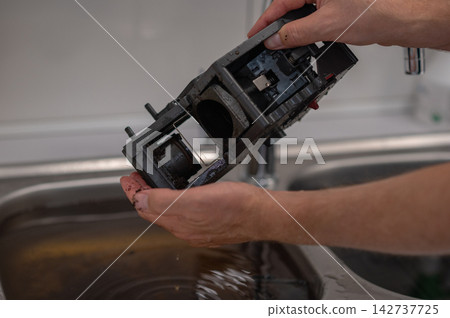 Hands holding disassembled coffee machine part over sink filled with water for cleaning process Hands holding disassembled coffee machine part over sink filled with water for cleaning process 142737725