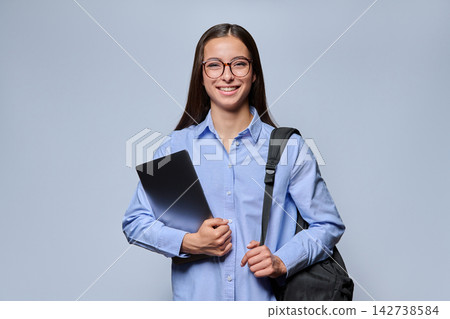 Smiling young woman student in glasses holding laptop and backpack studio shot 142738584