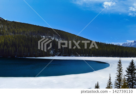 Winter landscape at Banff National Park, Canada, featuring a partially frozen lake surrounded by snow covered pine trees and Winter landscape at Banff National Park, Canada, featuring a partially frozen lake surrounded by snow covered pine trees and 142739110
